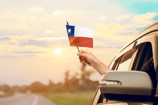 PERSONA HONDEANDO UNA BANDERA CHILENA DESDE LA VENTANA DE UN AUTO